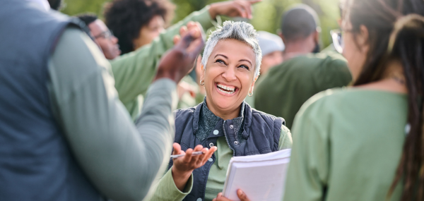 A woman with a clipboard smiles amongst a group of people she's helping