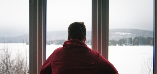 A photo of a man looking out of a window onto a winter scene