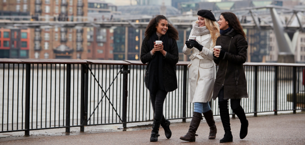 Three friends walk along the South Bank of the River Thames with coffee