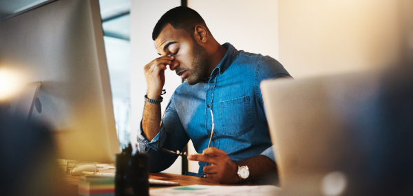 A man sits at his computer looking tired and overwhelmed