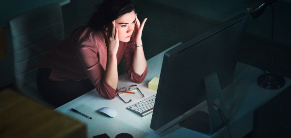 A woman sat in front of a laptop holds her fingers to her temples